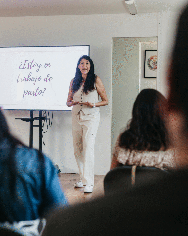 Bea Doula dando charla sobre señales de trabajo de parto frente a un grupo, con pantalla que dice "¿Estoy en trabajo de parto?"